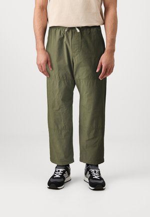 Olive green elastic waist pants with a relaxed fit, featuring stitched accents and a smooth texture, paired with black athletic shoes.