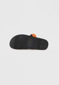Black rubber outsole with textured grooves and a slight heel. An orange synthetic strap is attached to the upper part of the shoe.