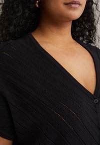Černý kardigan s texturovaným, žebrovaným designem. Má hluboký V-výstřih a jedno zapínání na knoflík vpředu.