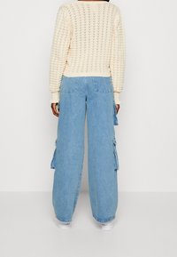 Light blue denim wide-leg cargo pants with large side pockets. The fabric is slightly faded, with a smooth texture and a relaxed fit.