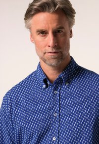 Niebieska koszula z guzikami, ozdobiona małym białym wzorem, z klasycznym kołnierzykiem i teksturowanym materiałem. Białe guziki uzupełniają całość.