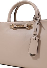 Borsa beige in pelle liscia con accessori in oro, logo "GUESS" impresso, due manici e un'etichetta removibile.