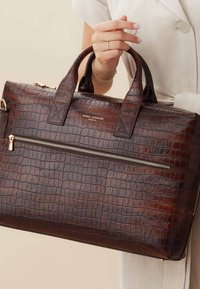 Bruine krokodillen-geperste leren tote bag met dubbele bovenhandvatten, een ritssluiting aan de voorkant en gouden hardware accenten.