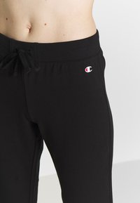 Schwarze Jogginghose mit elastischem Bund und Kordelzug, figurbetontem Design und kleinem, gesticktem Logo auf der linken Hüfte.