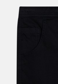 Zwarte denimstof met een voorzak, voorzien van contrasterend donkerblauwe stiksels langs de naden en de rand van de zak. Gladde textuur, aansluitend ontwerp.