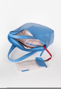 Borsa a mano in pelle blu con interno texturizzato, chiusura con zip e tracolla con accenti rossi. Include un piccolo portafoglio a fantasia attaccato.