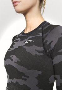 Zwart en grijs camouflage sporttop met lange mouwen, een strakke pasvorm, ribbelstructuur en een klein wit logo op de borst.