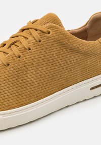Brune suède sneakers med vertikale ribbet tekstur, rund tå og hvit gummisåle. Har matchende snøringer og minimale sømdetaljer.