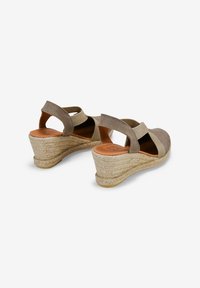 Sandalias de cuña de esparto en ante taupe con correas elásticas, talón abierto y suela de yute trenzado. Cuenta con una plantilla de cuero suave.