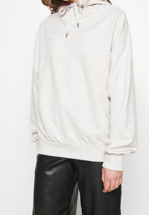 Vaaleanharmaa huppari, jossa on kiristysnyörit, pitkät hihat ja resorit hihansuissa, yhdistetty mustiin nahkahousuihin, ihmisen yllä yksinkertaisella taustalla.