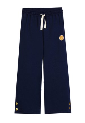 Pantaloni a gamba larga color blu navy con vita elastica, coulisse crema, bottoni dorati vicino all'orlo e piccolo logo circolare arancione sulla coscia destra.