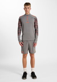 Helles graues Sportoutfit mit einem Langarmoberteil mit gemusterten Ärmeln und kurzen Shorts. Akzente in leuchtendem Orange. Texturiertes, sportliches Design.