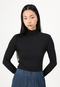 Svart ribbestrikket turtleneck topp kombinert med en plissert blå skjørt. Tøyet ser mykt ut med en tettsittende silhuett og lange ermer.