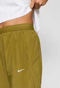 Λαδί σορτς με ελαστική ζώνη, πλαϊνές τσέπες και λευκό λογότυπο Nike. Το ύφασμα φαίνεται ελαφρύ και λείο.