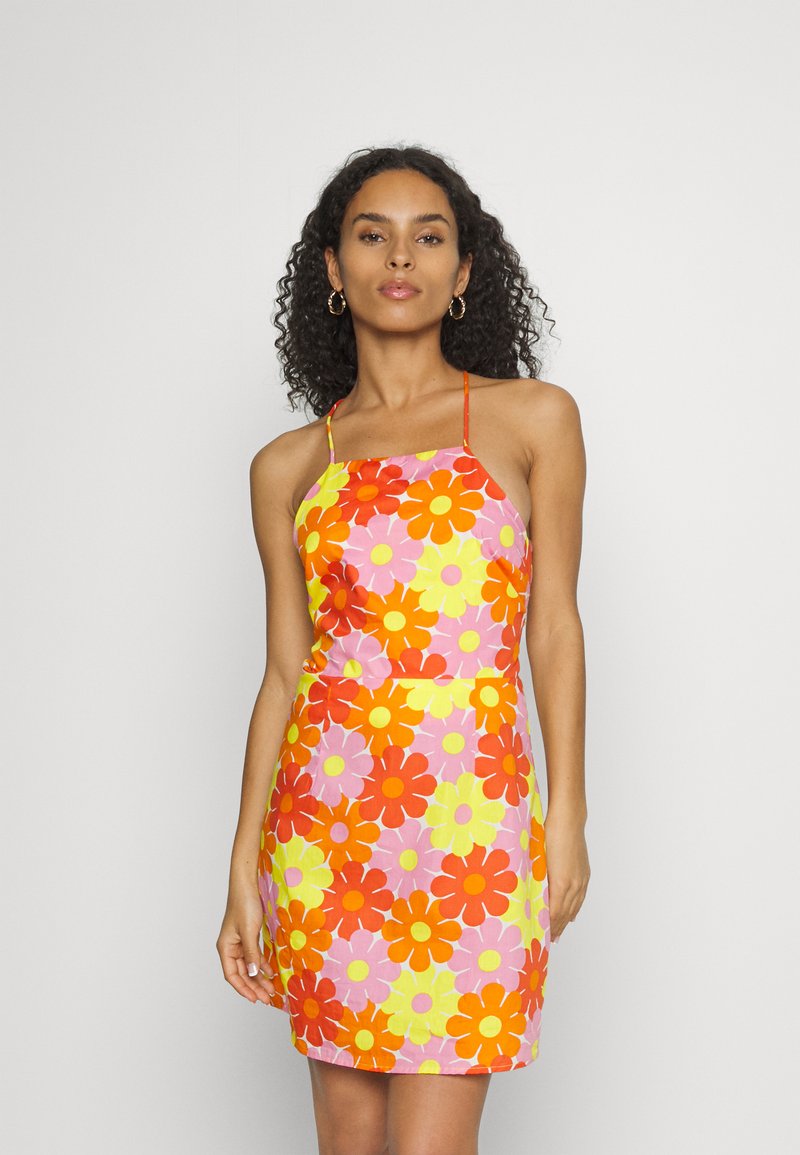 Vestido floral colorido com grandes flores laranja e amarelas sobre um fundo rosa. Alças finas com um corte ajustado e comprimento até aos joelhos.