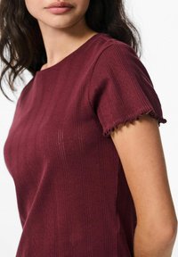 Bordeaux kortärmad topp med en texturerad yta med vertikala ränder och scallopade kanter på ärmsluten.