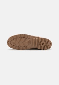 Suela de zapato de goma en marrón claro. Presenta un patrón de taco con ranuras e indentaciones circulares para mayor tracción. Textura duradera.
