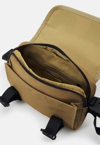 Beige Schultertasche aus Stoff mit Reißverschluss, Innenfach und verstellbaren schwarzen Trägern. Glatte Textur und robuste Verarbeitung.