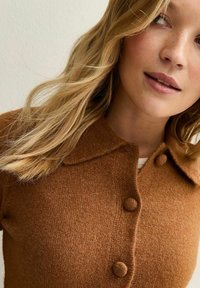 Cardigan marrone in morbido tessuto a maglia, con colletto, chiusura a bottoni e finitura testurizzata. Leggera lucentezza e vestibilità favorevole.