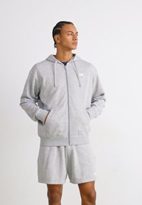 Grå lynlås hoodie lavet af blødt stof, med hætte, frontlommer og ribbet kant. Sammen med matchende shorts, enkel logo detalje.