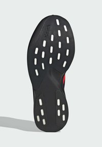 Black shoe sole with white traction dots, featuring a textured surface and curved edges, displaying a logo near the heel.