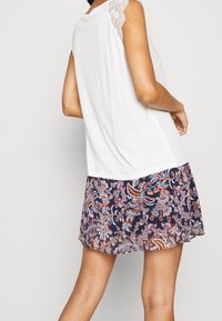 Bílý top s krajkovým akcentem na rameni, zkombinovaný s námořnickou sukni s barevným květinovým paisley vzorem. Hladká tkanina, volný střih.