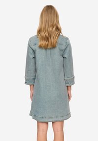 Světle modré džínové šaty s tříčtvrtečními rukávy, nabraným zády a surovým okrajem. Disponují prošíváním a volným střihem.