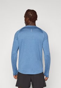 Langermet trenings skjorte i lyseblått stoff, med rund hals, flate sømmer og en liten logo detalj på øvre rygg.