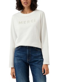 Kremowa bluza z długim rękawem z napisem "MERCI" w dekoracyjnych akcentach, zestawiona z ciemnoniebieskimi dżinsami, prezentująca swobodny fason.