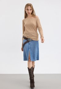 Beige ribbet langermet topp parret med et blått denimskjørt med en frontspalte og et brunt dekorativt belte. Sorte cowboystøvler fullfører antrekket.