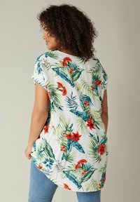 Blumen-Tunika mit einem lebhaften Druck von roten Blumen und grünen Blättern auf einem weißen Hintergrund; kurze Ärmel und ein abgerundeter Saum.