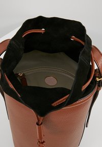 Borsa bucket in pelle marrone con interno in suede nero, dotata di chiusura a coulisse e una tasca interna con zip con un'etichetta rotonda firmata.