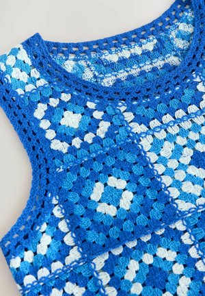 Top en crochet avec un motif géométrique de pièces bleues et blanches. Le matériau a une apparence texturée avec des détails ajourés.