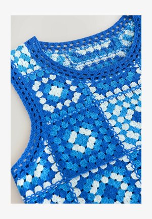 Top all'uncinetto con un motivo geometrico di pezzi blu e bianchi. Il materiale ha un aspetto texturizzato con dettagli in pizzo.