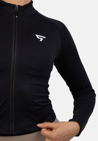 Zwarte sportjacket met rits gemaakt van rekbaar materiaal, met een strakke pasvorm en een witte logo-accent op de borst.