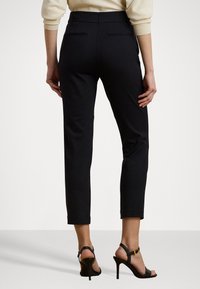 Černé tailored kalhoty s úzkým střihem, které mají středně vysoký pas, zadní kapsy a zkrácenou délku. Nošeny s černými vysokými sandály.