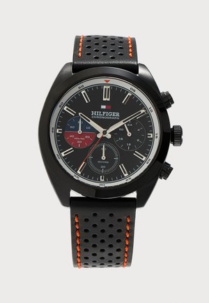 Μαύρο chronograph ρολόι με μαύρο δερμάτινο λουράκι με τρύπες, πορτοκαλί ραφές και τρεις υποκαντράν που δείχνουν δευτερόλεπτα, λεπτά και 24ωρη ώρα.