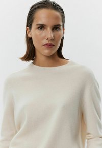 Pullover in maglia di colore crema chiaro, con collo a girocollo a coste, texture morbida, maniche lunghe e dettagli di cucitura sottili sulle spalle.