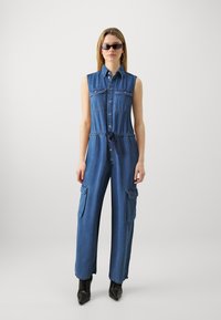 Jeansdress med ermene design, trykknapper, to brystlommer, justerbar midje, cargo-lommer på siden og vid ben.