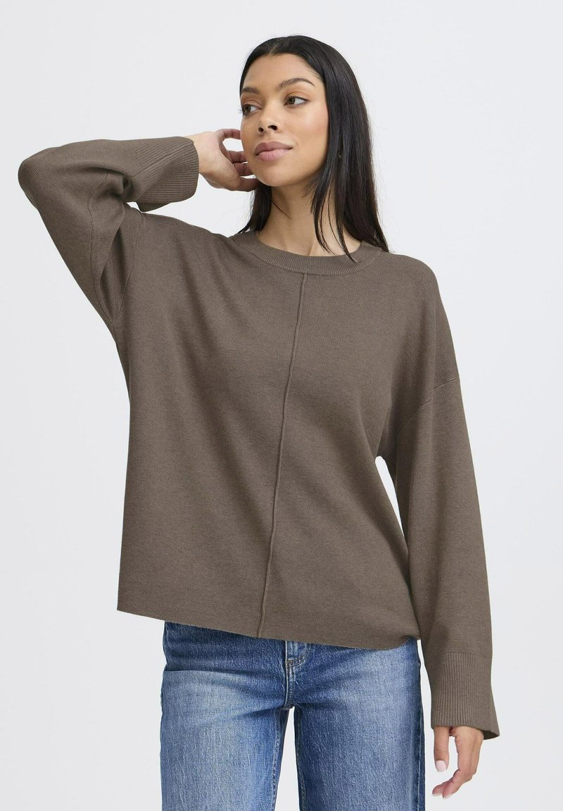 Pull en maille marron avec un col rond, des épaules tombantes et des poignets côtelés. Le matériau semble doux avec une coupe décontractée, associé à un jean bleu.