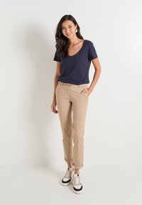 T-shirt bleu marine à col en V, pantalon beige ajusté, ceinture beige et baskets crème avec des accents noirs. Tissu lisse, silhouette ajustée, style décontracté.