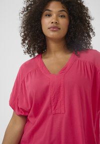 Top rosa a maniche corte con scollo a V e dettagli plissettati sul davanti. Realizzato in tessuto morbido con una vestibilità comoda e una superficie liscia.