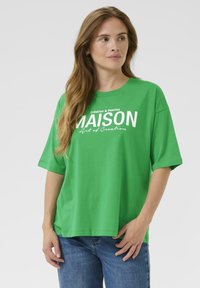 Zielona bawełniana koszulka z luźnym krojem, z białym nadrukiem graficznym z napisem "MAISON" oraz dodatkowym tekstem. Krótkie rękawy i okrągły dekolt.