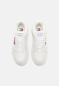 Sneakers bianchi con una tomaia in pelle liscia, punta traforata, chiusura con lacci e suola in gomma. Accenti rossi e blu nel design.