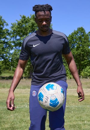 Must Nike spordisärk hallide aktsentidega, sinised Paris Saint-Germaini dressipüksid, välitingimustes sinise ja valge mustriga jalgpalli tasakaalustades.