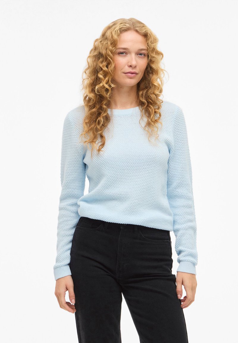 Ανοιχτό μπλε πλεκτό πουλόβερ με υφή, στρογγυλή λαιμόκοψη και μακριά μανίκια, συνδυασμένο με μαύρο παντελόνι. Σχεδιασμός σε κανονική εφαρμογή.