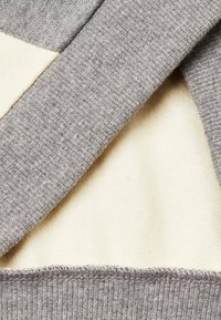 Il tessuto grigio a coste sovrasta il materiale morbido color crema, evidenziando un design a strati con cuciture ordinate sul bordo.