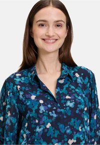 Blauwe en groene gebloemde blouse met een kraag en knoopsluiting aan de voorkant, met een gladde, zijdezachte textuur en lange mouwen.