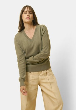 Olijfgroen v-hals pullover met lange mouwen, structuurstof en geribbelde zoom, gecombineerd met beige high-waisted broeken.