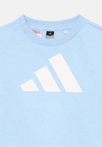 Ανοιχτό μπλε φούτερ με λευκό λογότυπο adidas. Διαθέτει στρογγυλή λαιμόκοψη και ριμπ γιακ ά. Το υλικό φαίνεται μαλακό με ομαλή υφή.